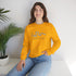 Woman wearing a yellow sweatshirt with a design and text, sitting on a white surface with a plant in the background.